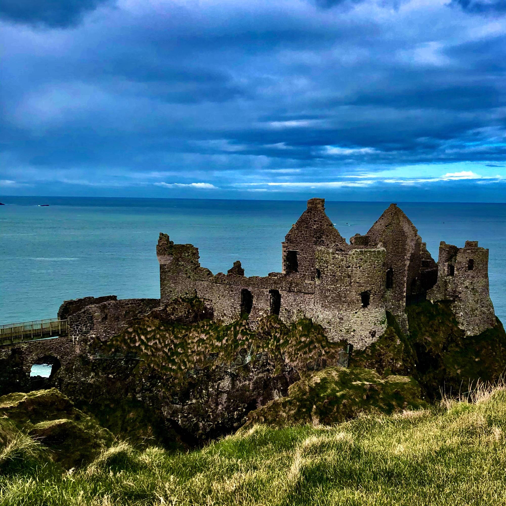 Photograph of ruins in Ireland against a bright blue sky and water.
